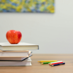 books stacked on a desk with an apple next to pens and blocks