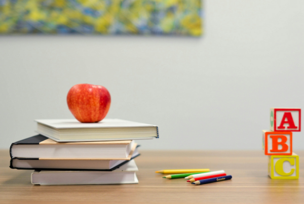 books stacked on a desk with an apple next to pens and blocks