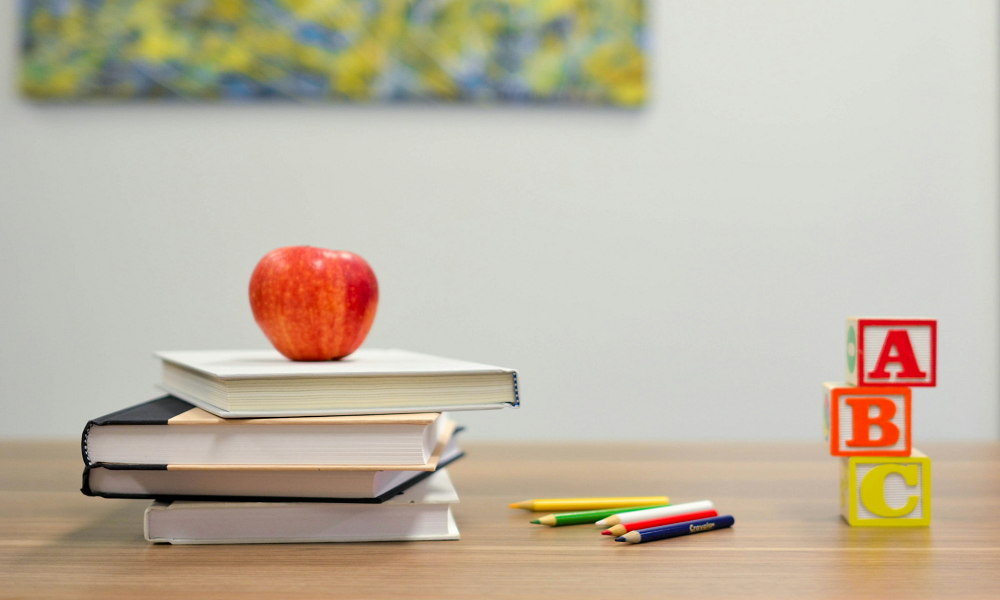 books stacked on a desk with an apple next to pens and blocks